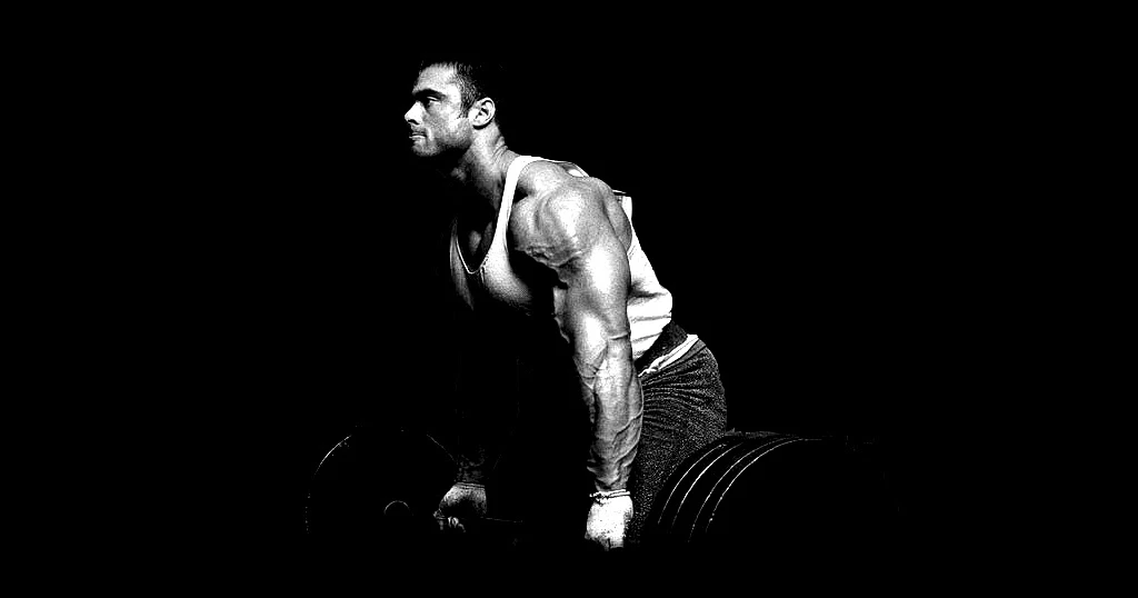 Diese eindrucksvolle Schwarz-Weiß-Fotografie zeigt den professionellen Bodybuilder Frank McGrath bei der Ausführung einer vorgebeugten Langhantelruderübung. Das Bild ist bekannt für seinen intensiven, kontrastreichen „Blood & Guts“-Stil.