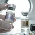 Pharmavial unter klinischem Licht neben gefälschtem Gegenstück mit verschwommenem Hologramm – Sichtprüfung und Reagenztest-Kit zur Identifikation gefälschter und unterdosierter Steroide
